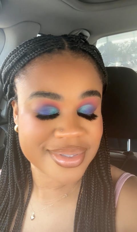 Close-up of a woman with braided hair and colorful blue and pink eyeshadow makeup in a car