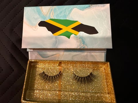 Pair of golden glittery false eyelashes in an open box with Jamaican flag design on the lid