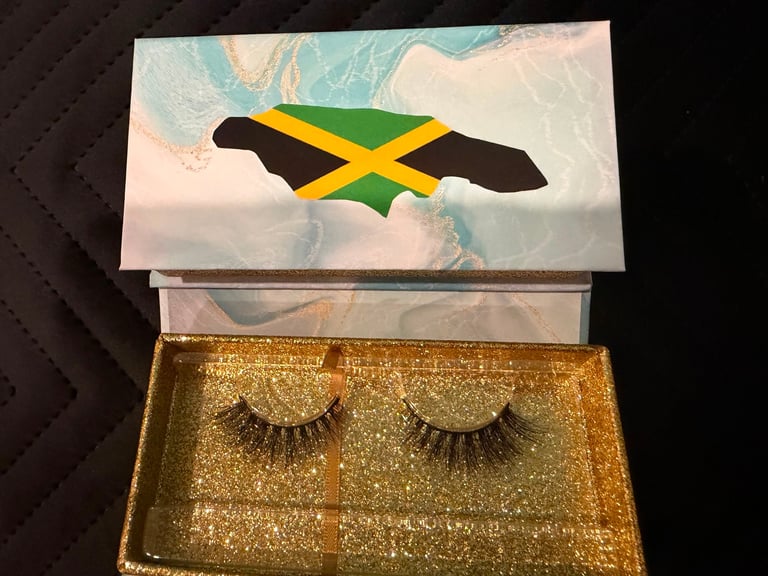 Pair of golden glittery false eyelashes in an open box with Jamaican flag design on the lid