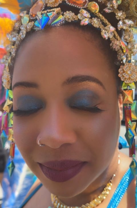 Woman with blue eyeshadow and burgundy lips wearing an ornate multicolored beaded headwrap and gold jewelry