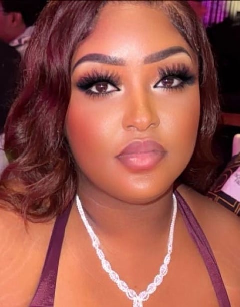 Woman with burgundy waves, bold eye makeup with long lashes, nude lipstick, and crystal necklace at indoor event